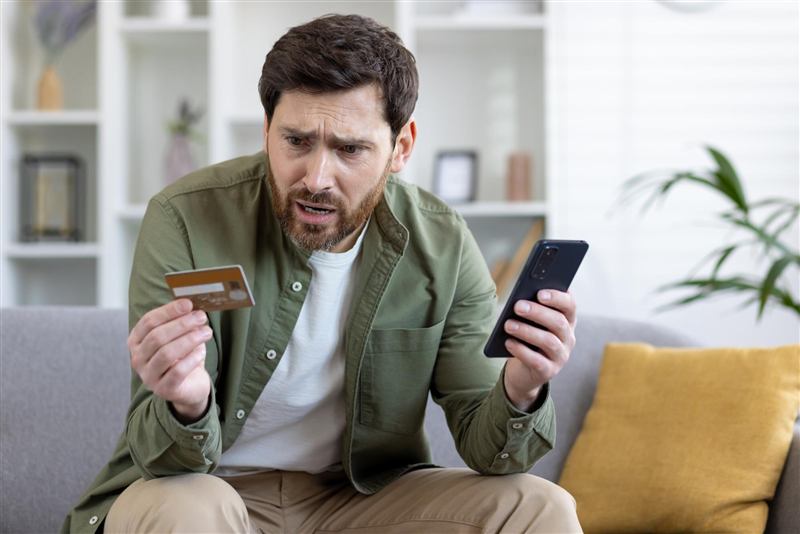 Homem preocupado com cartão de crédito e celular após uma fraude bancária