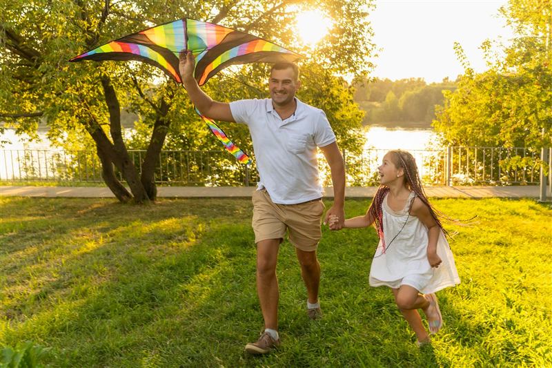 Pai e filha soltando pipa em um parque ao pôr do sol