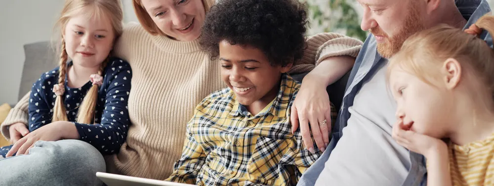 Pai, mãe e três crianças sorrindo juntos no sofá de casa