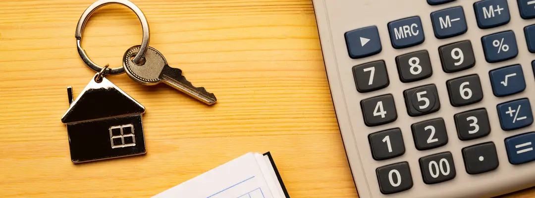 Chave com chaveiro em forma de casa, calculadora e caderno de anotações sobre a mesa