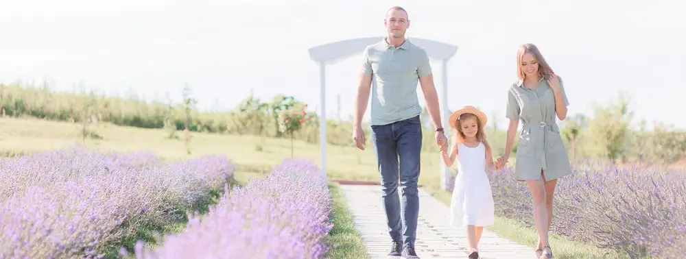 Pai e mãe caminhando de mãos dadas com a filha em um caminho de jardim