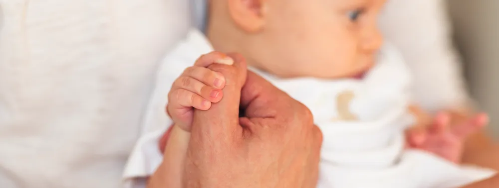Mão de adulto segurando a mão de um bebê