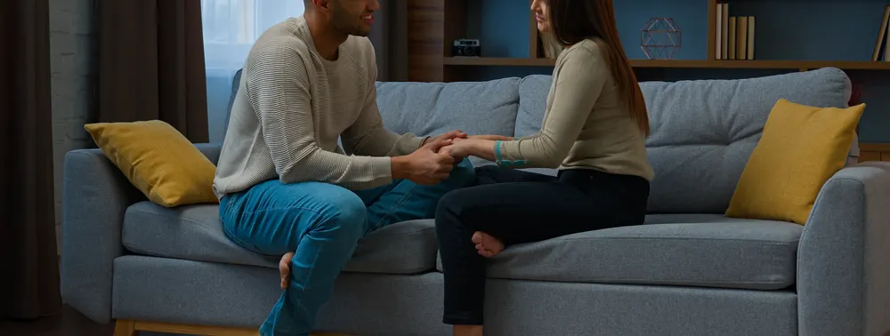 Casal sentado no sofá de casa, de mãos dadas, conversando