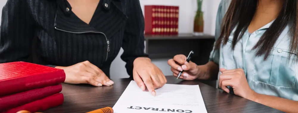 Duas mulheres conferindo um documento sobre a mesa, com calculadora e martelo de juiz