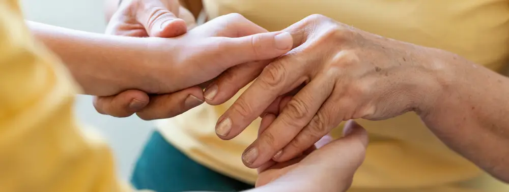 Mãos de uma pessoa jovem segurando as mãos de uma pessoa mais velha
